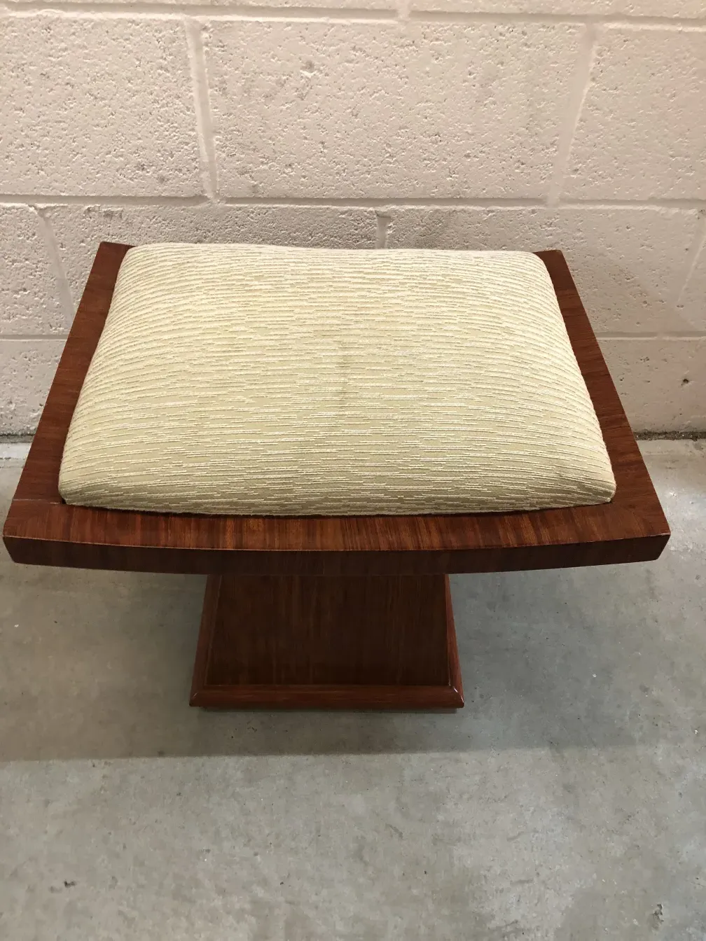 Antiker Hocker mit beigem Kissen in neutralem Umfeld.