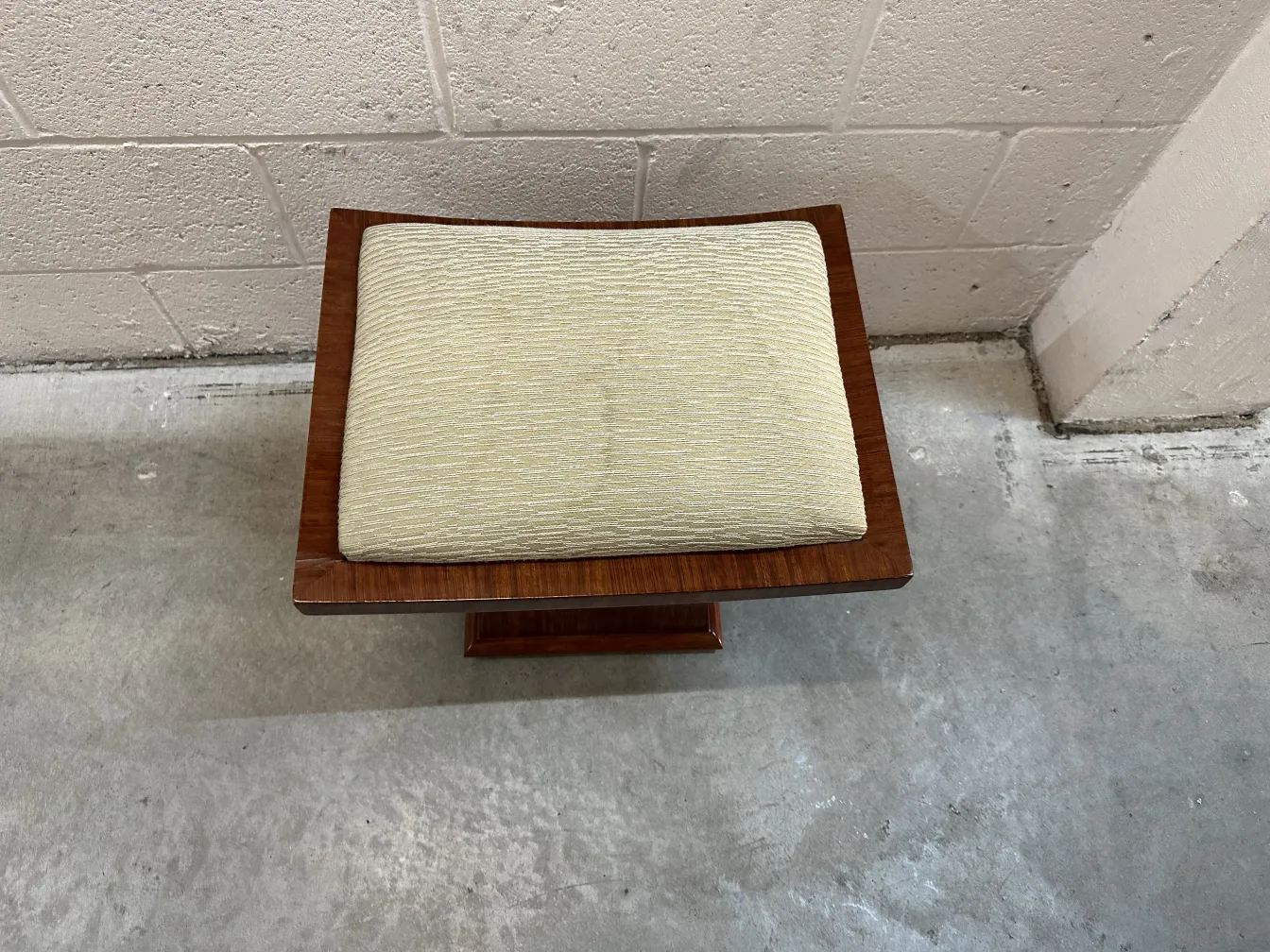 Antigua banqueta con cojín crema y diseño clásico.