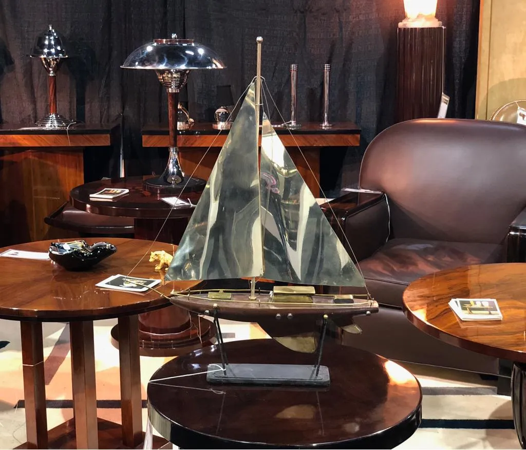 Mesita antigua con un barco decorativo y lámparas en el fondo.