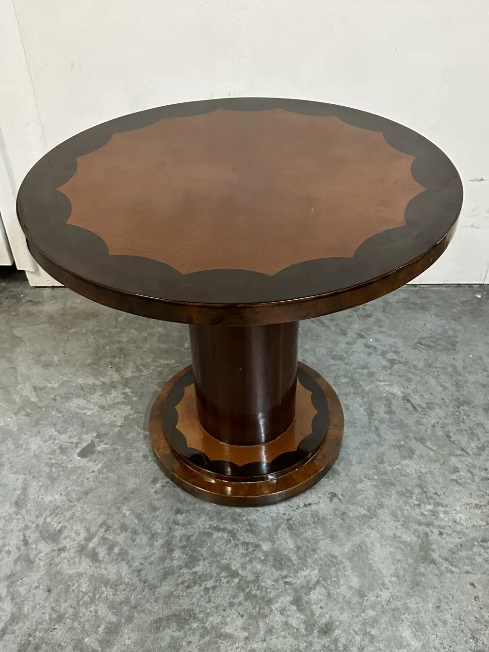 Tavolino antico rotondo con base decorativa in un ambiente neutro.