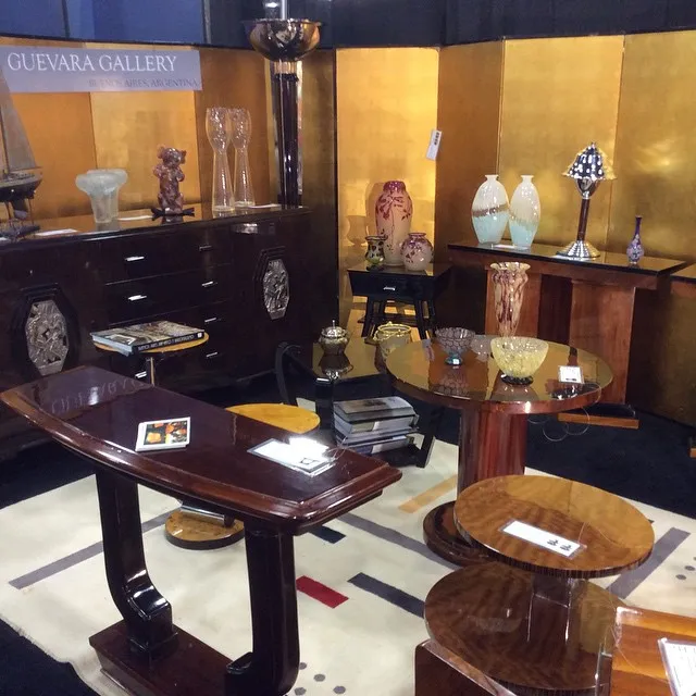 Mesita antigua con un diseño bonito, en un ambiente de galería, rodeada de otros objetos decorativos.