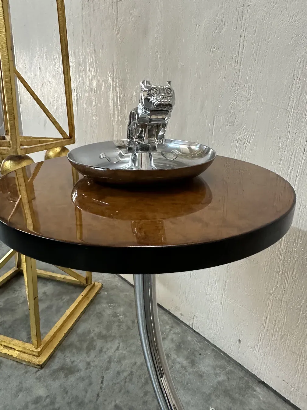 Petite table ancienne avec un design circulaire et un objet décoratif dessus, sur un sol texturé.