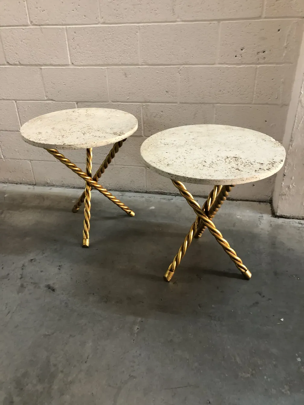 Zwei antike kleine Tische mit runden Oberflächen und goldenen Beinen in einem neutralen Ambiente.