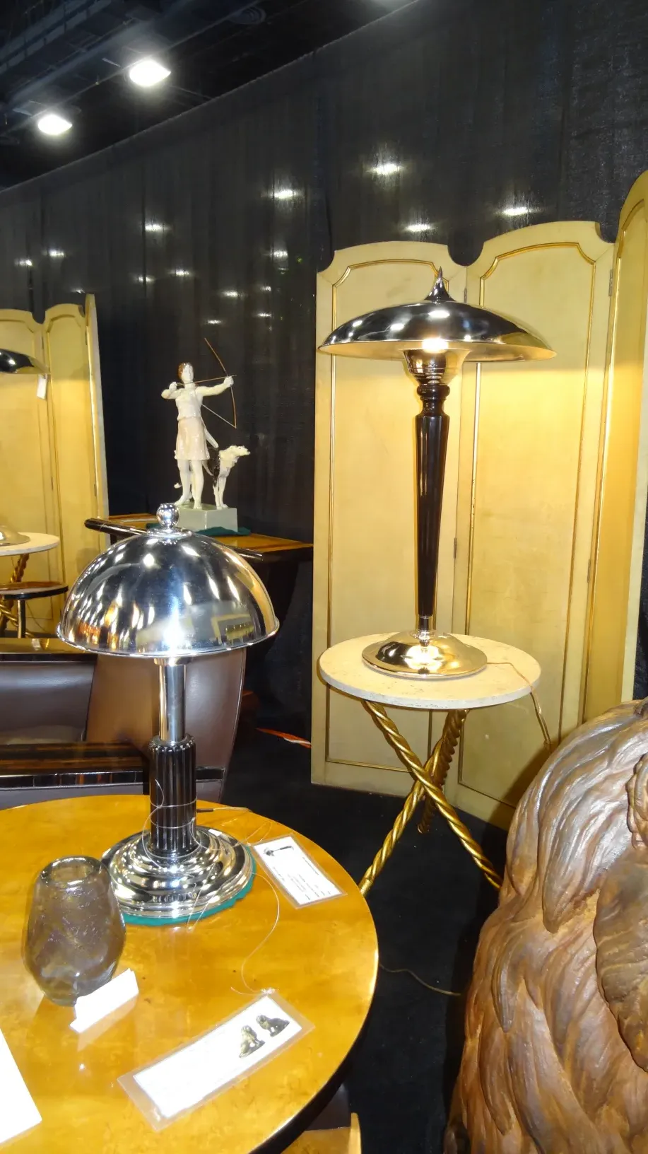 2 tavolini antichi in un ambiente decorativo, con una lampada e una figura sullo sfondo.