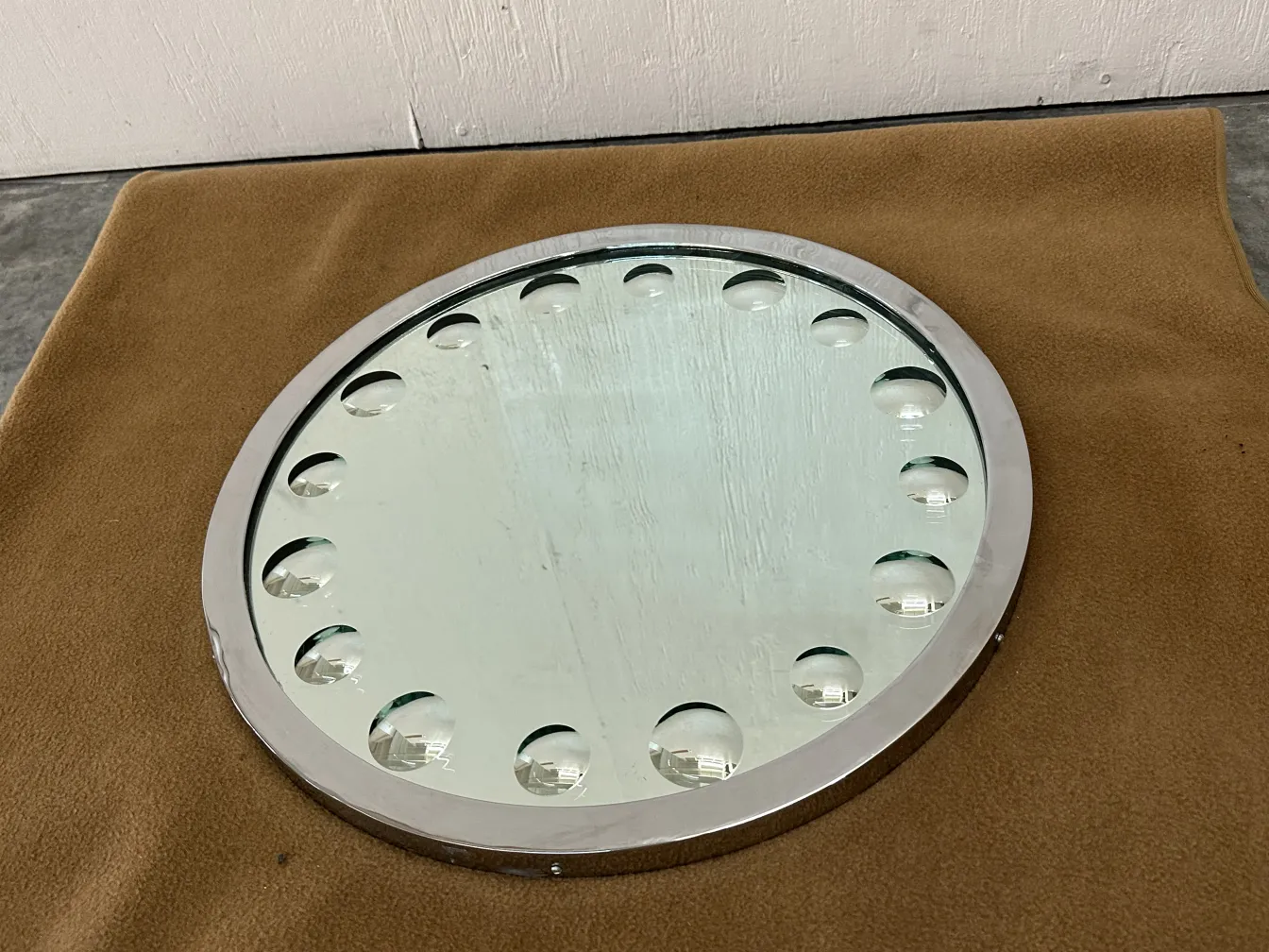 Round antique mirror with edge details, placed on a soft surface.