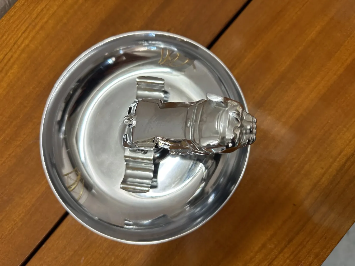 Cendrier ancien avec une figure décorative en haut et une base brillante.