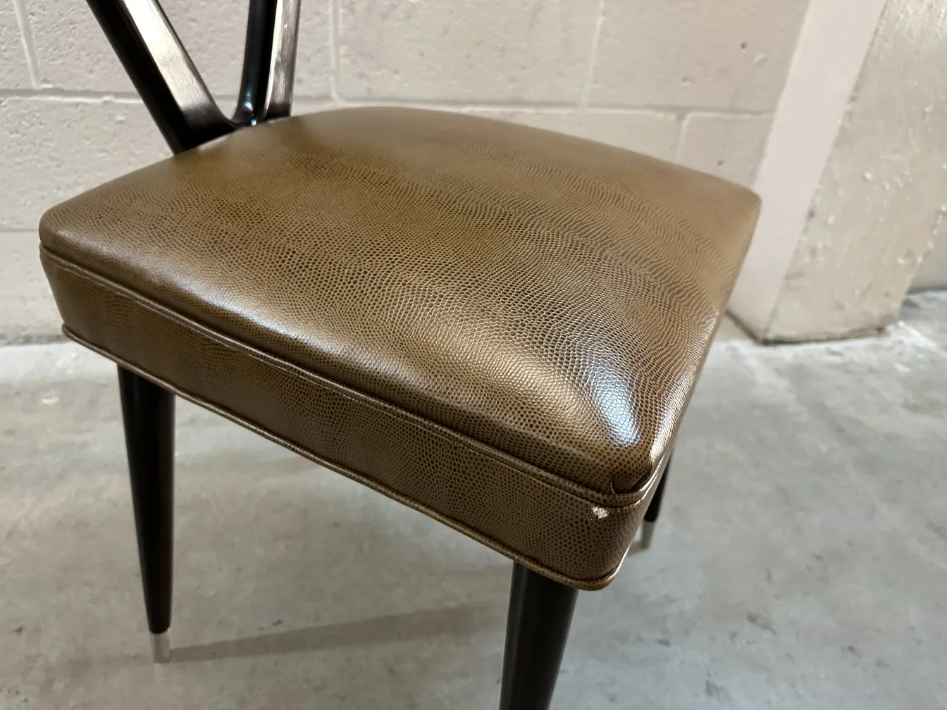 détail d'une chaise antique carlo mollino avec des pieds noirs et un siège marron