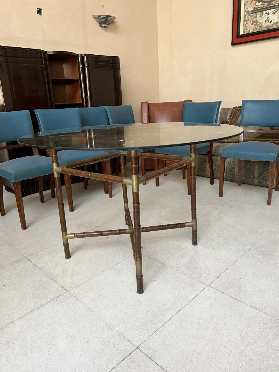 Tavolo da pranzo antico con base decorativa, circondato da sedie blu in un ambiente accogliente.