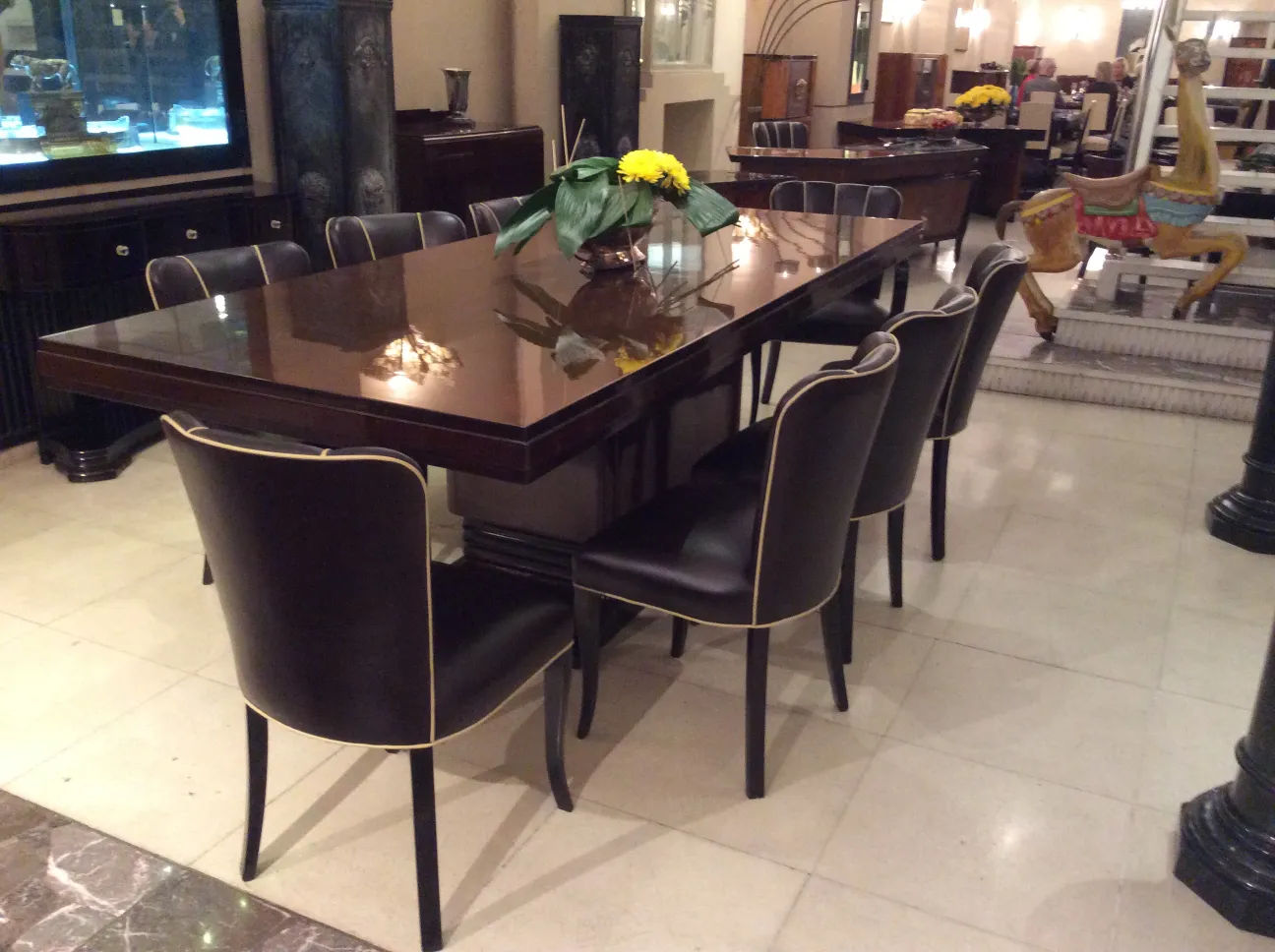 Mesa de comedor antigua con ocho sillas, decorada con flores. Ambiente elegante.