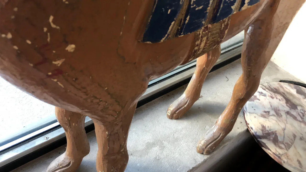 Antique llama sculpture with decorative details, situated by a window.