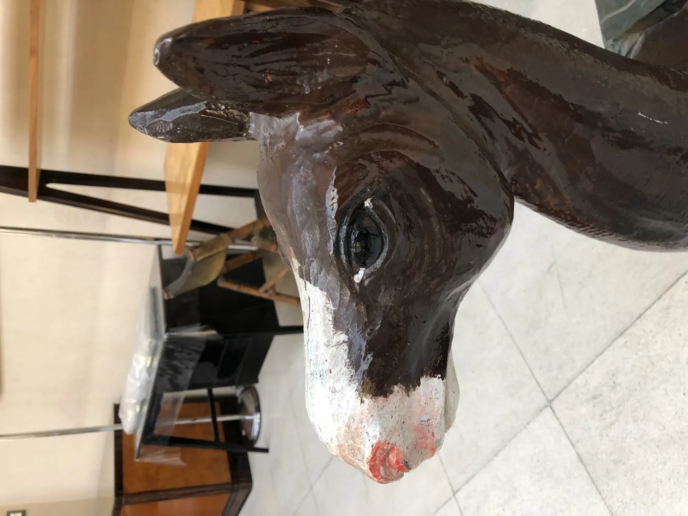 cabeza de antigua llama en cerámica con detalles decorativos. Fondo de muebles variados.