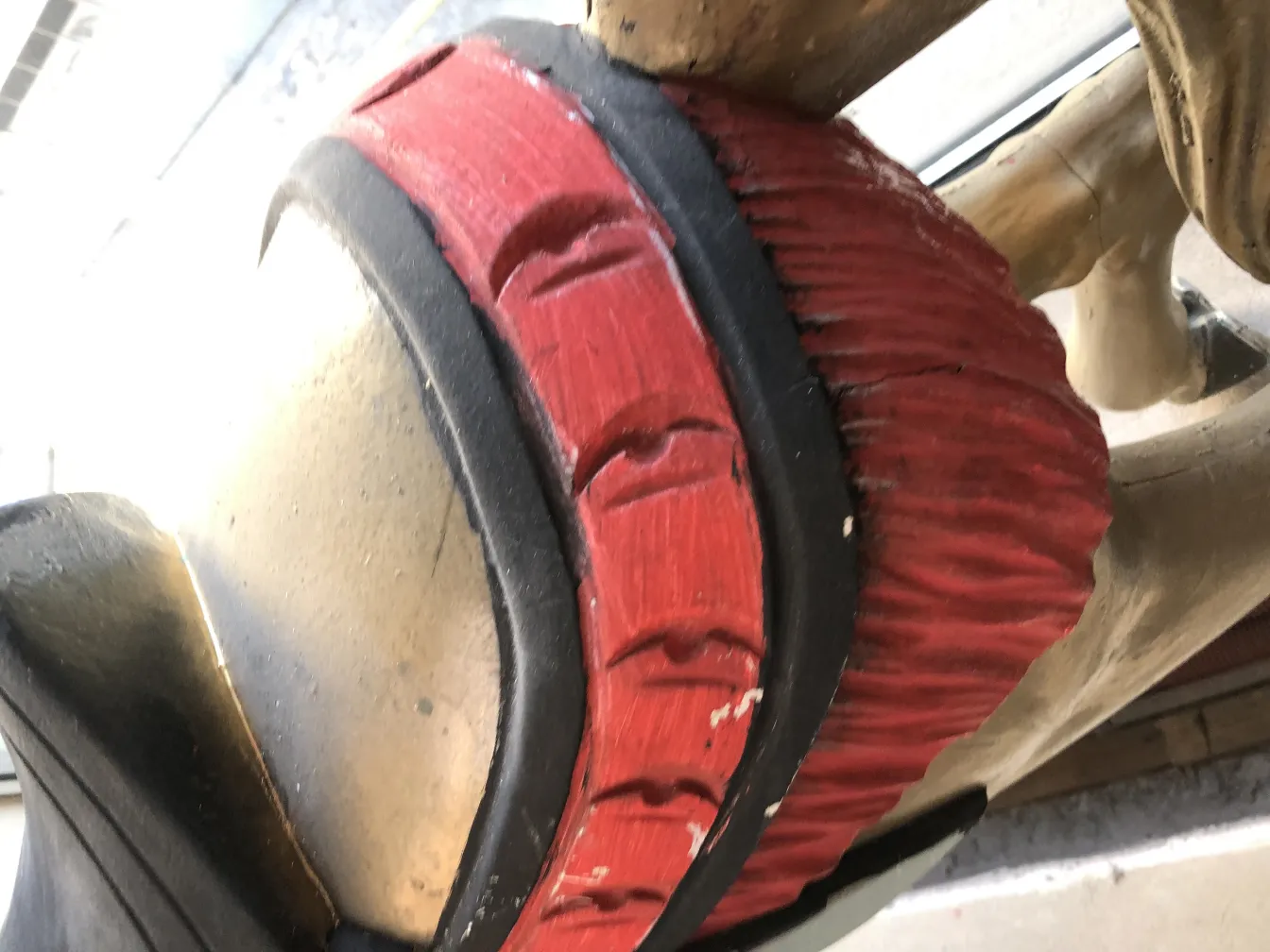 Estatuilla antigua de unicornio con detalles rojos y negros, fondo neutral.