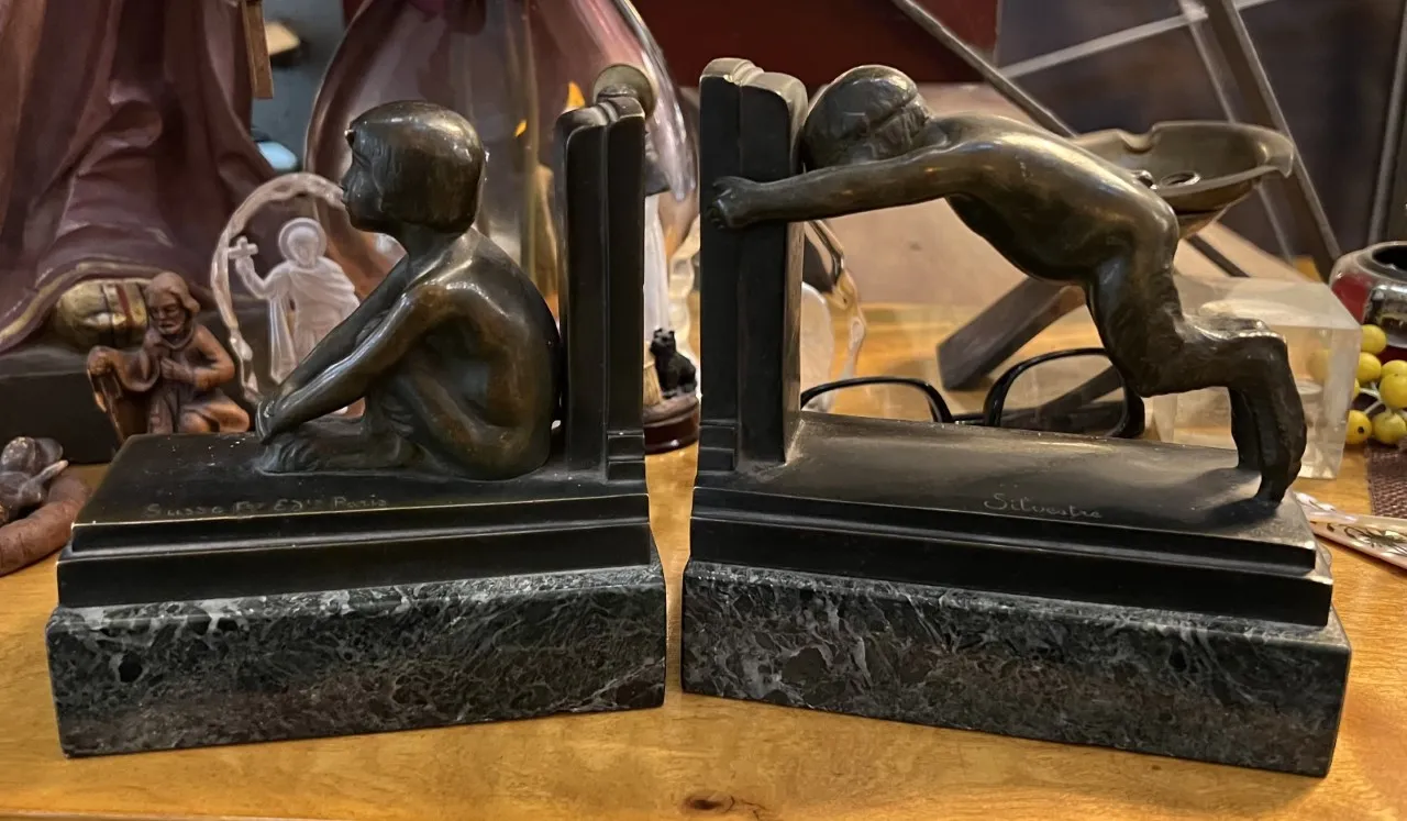 Fermalibri antichi con sculture di bambini in bronzo, circondati da oggetti decorativi.