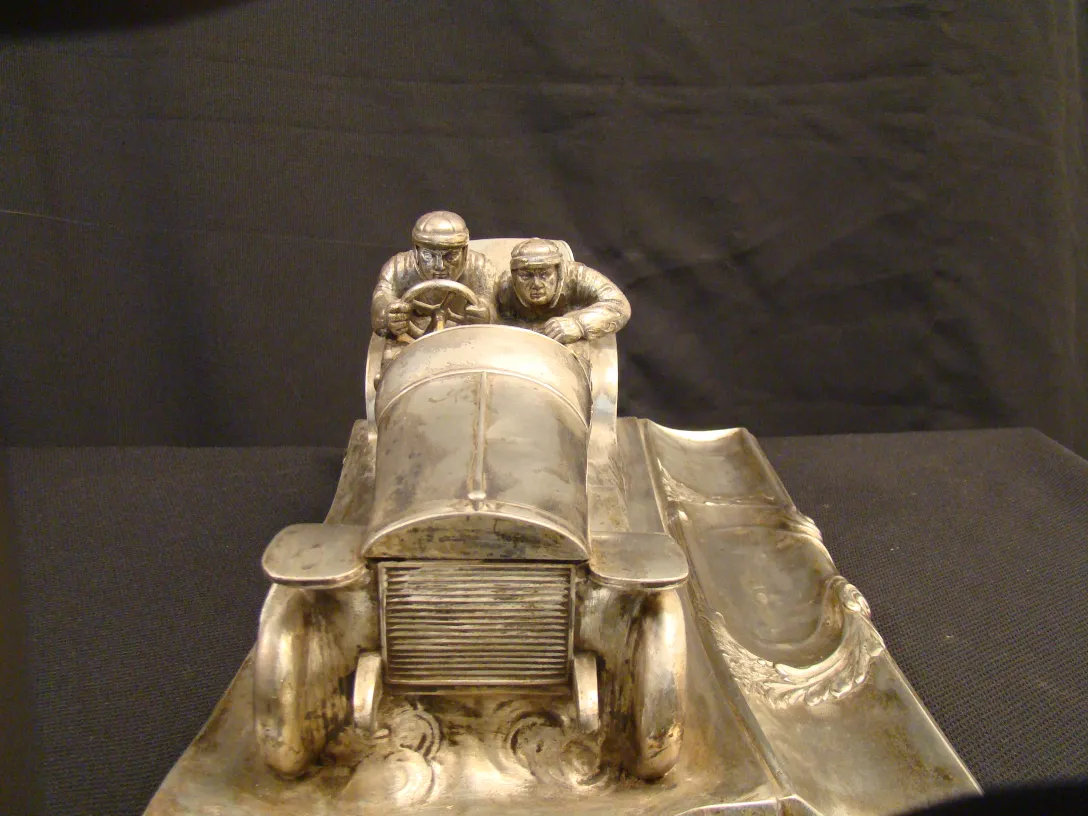 tintero antiguo representando un coche de carreras con dos pilotos, detalles en metal brillantes