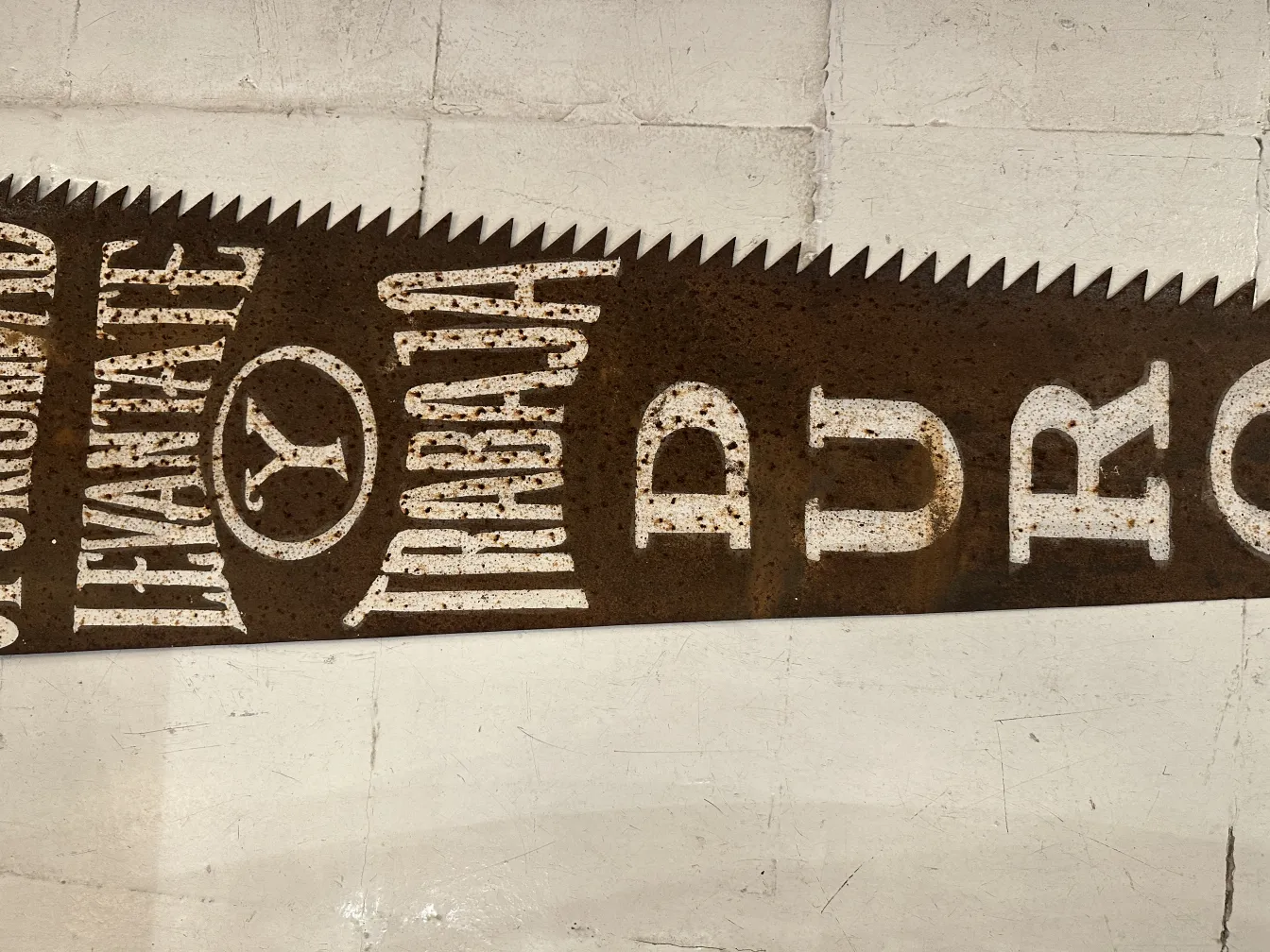 Antique advertising hand saw with white inscriptions on a rusty background