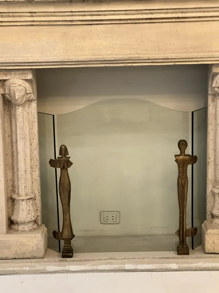 frente de chimenea antiguo con figuras del artista alberto giacometti, en ambiente interior. figuras estilizadas a cada lado.