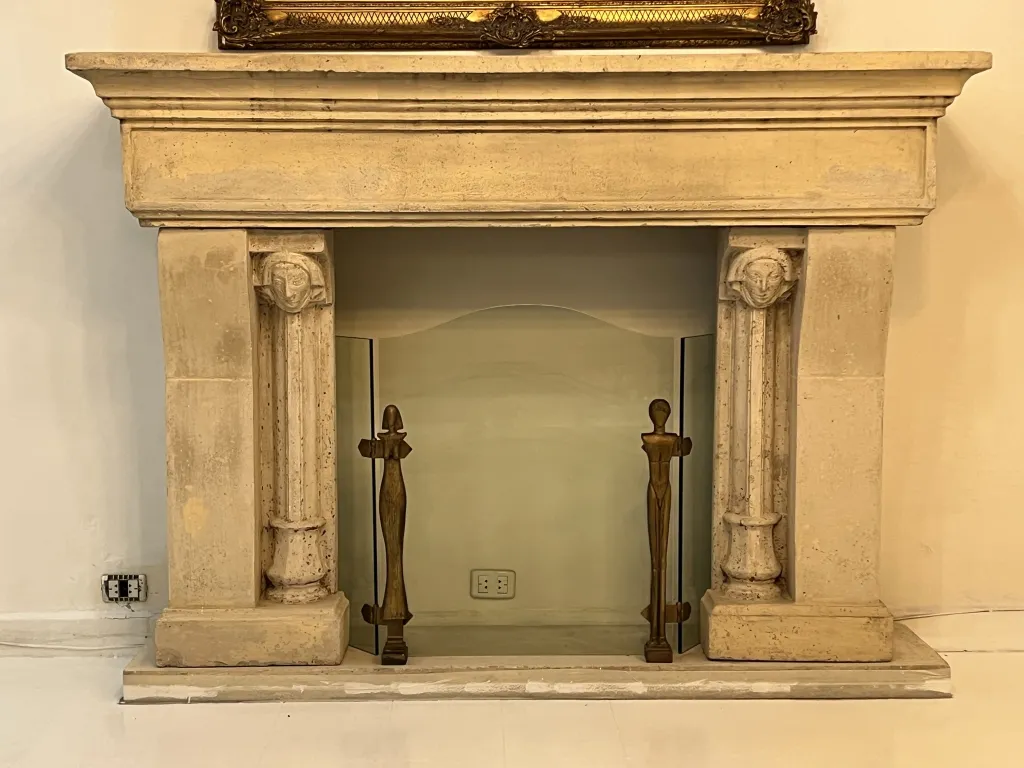 Cornice del camino antico con dettagli e decorazioni, include figure di Alberto Giacometti, atmosfera accogliente.