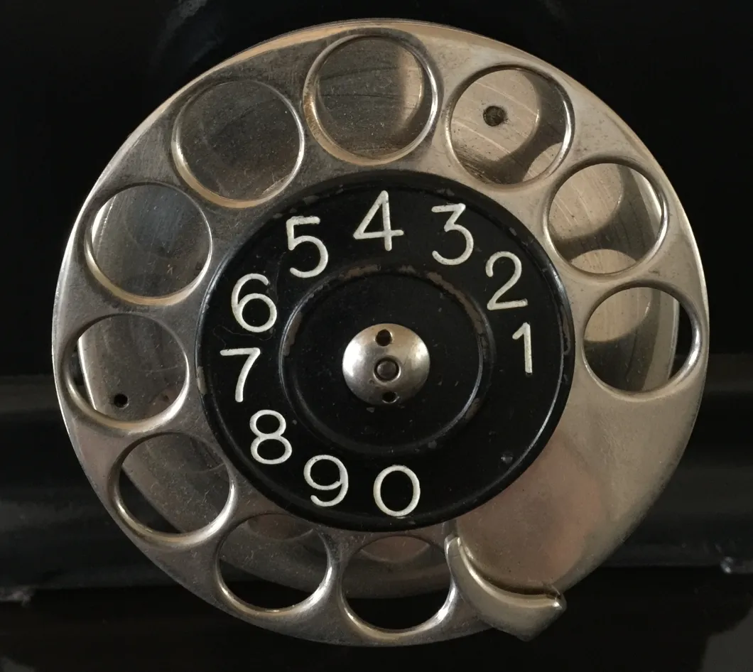 Vista dall'alto di un telefono antico con disco rotante, dettagli in nero e argento.