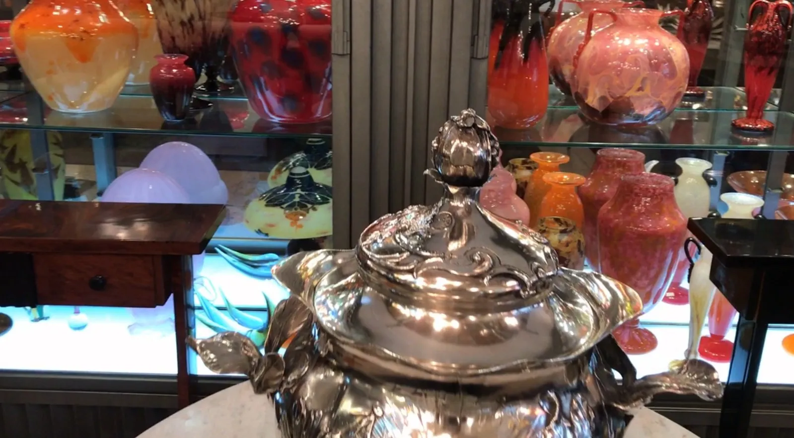 Dekorative WMF Bowle mit komplizierten Designs und bunten Vasen im Hintergrund.