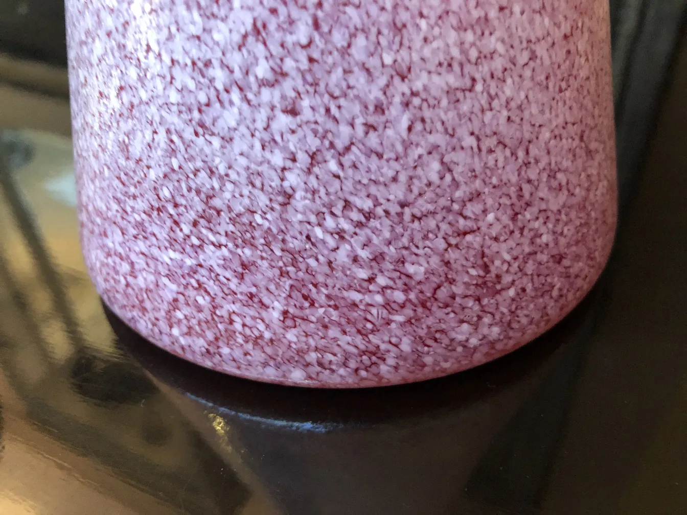 Antique decorative vase in pink with a textured surface, set on a dark surface.