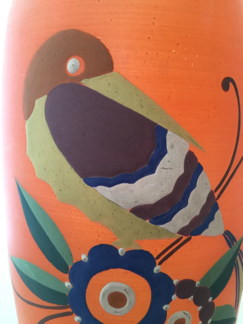 Vaso de flores antigo com design colorido de aves e flores, fundo liso.