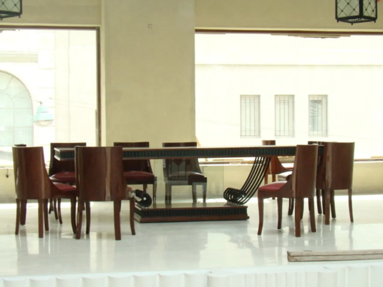 Старинный обеденный стол в светлом помещении, окружённый стульями.