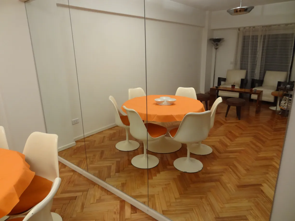 antique dining table for 7 people in a cozy setting with white chairs and an orange tablecloth.