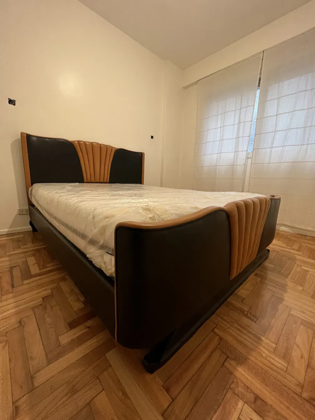 Letto antico Art Deco con testata in tonalità scure e chiare, ambiente caldo.