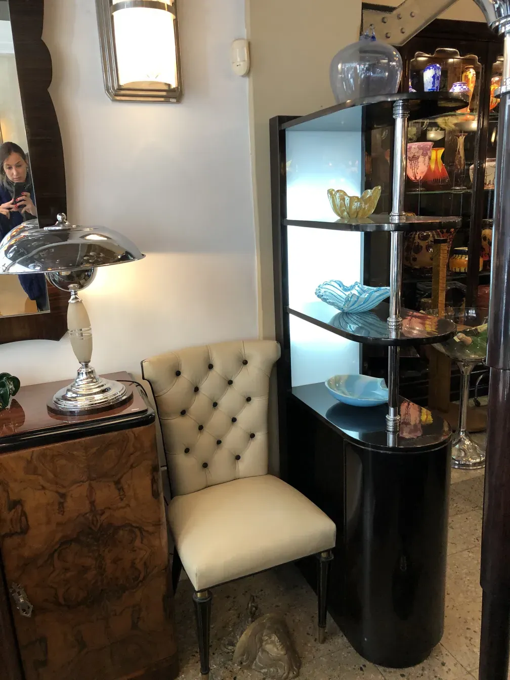 Meuble à cocktail ancien avec des objets en verre colorés et une chaise blanche.