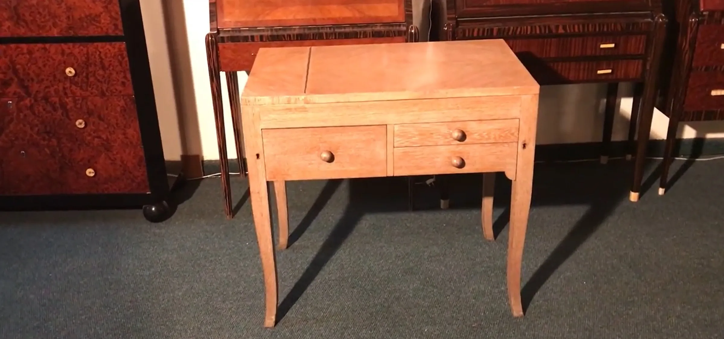 Antique light wood desk with rounded drawers, dark background.