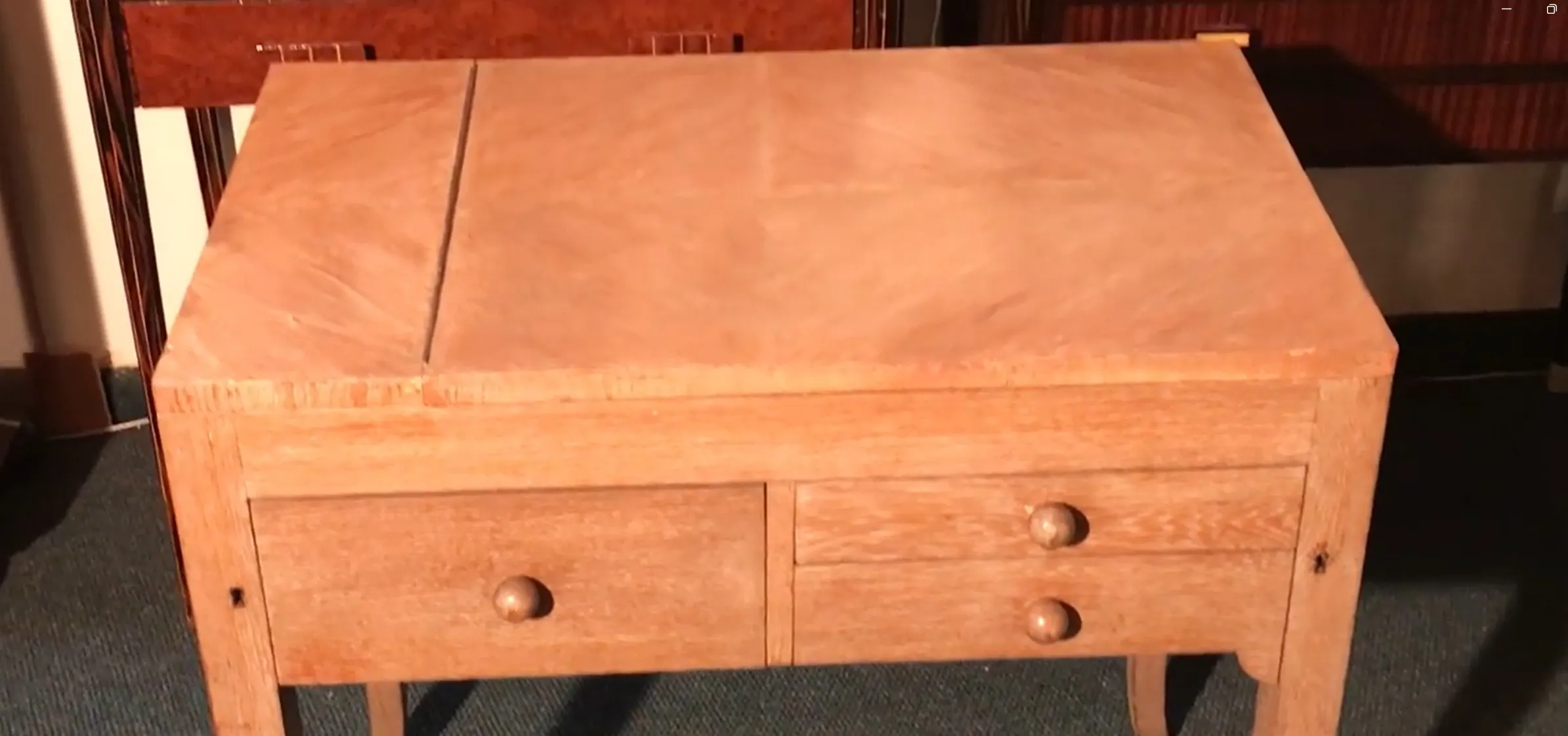 Antiker Schreibtisch aus hellem Holz mit zwei abgerundeten Schubladen in einer sanften Umgebung.