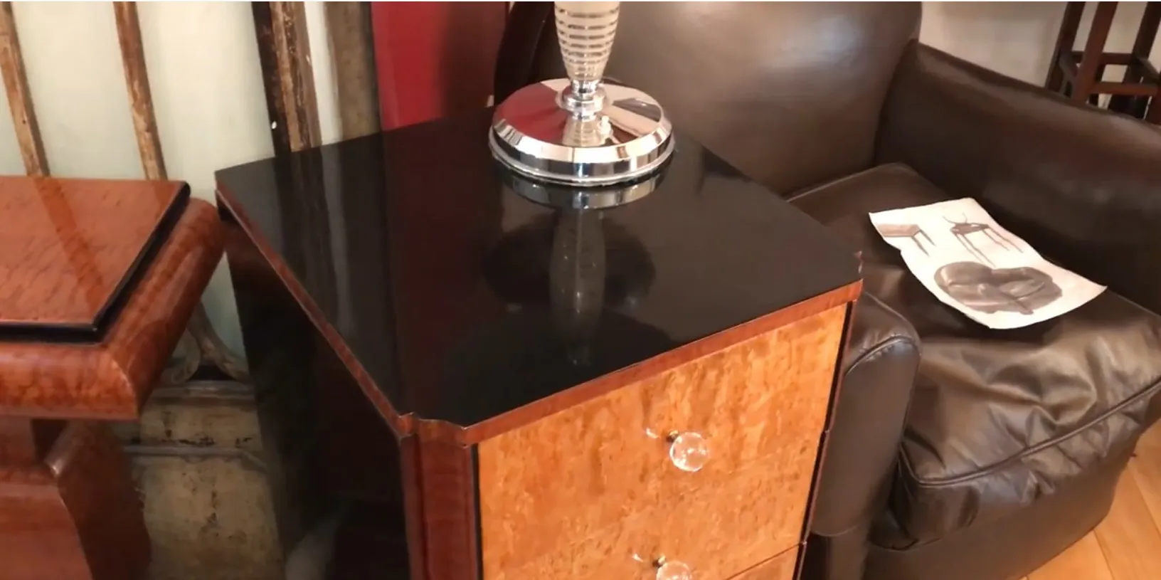 Commode ancienne en bois avec finition brillante et poignées en cristal, à côté d'un canapé marron.