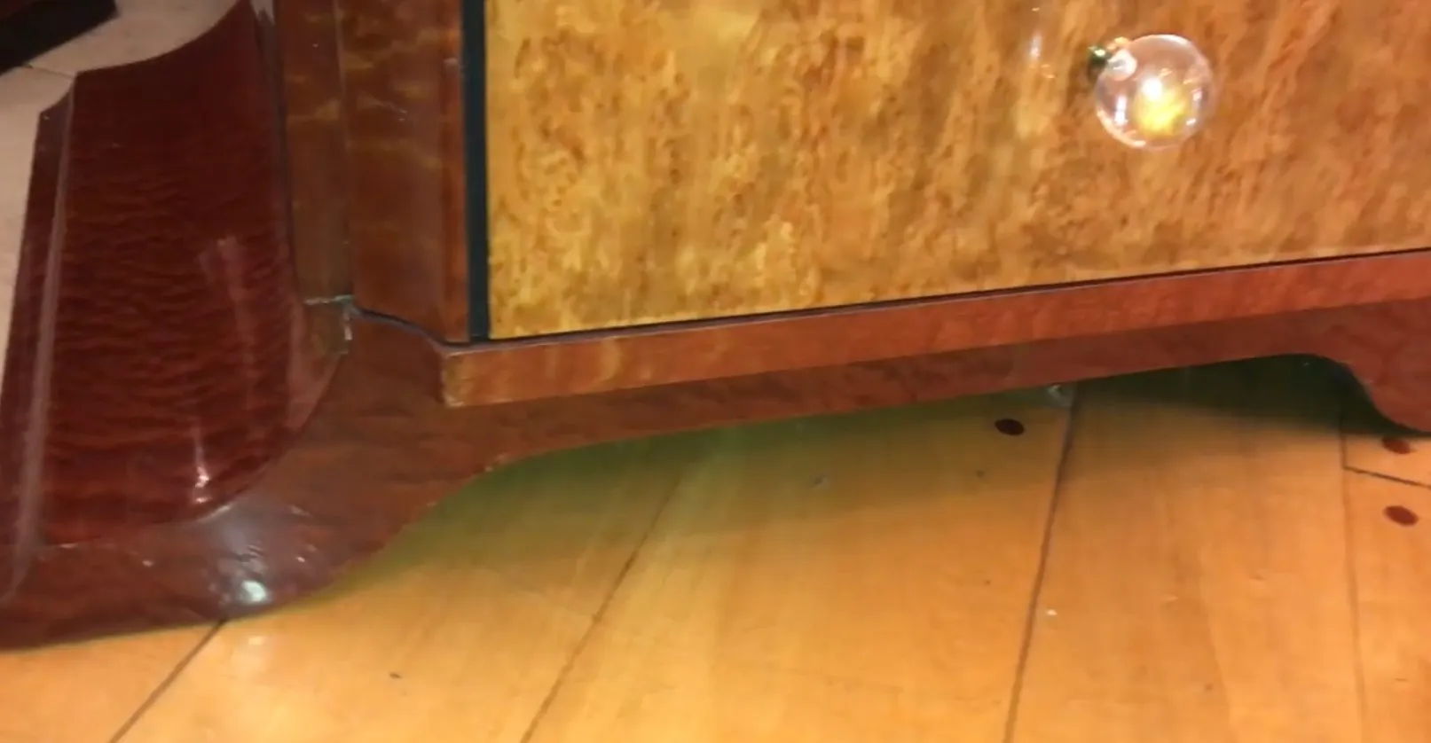 détail d'une commode ancienne avec un design élégant et une poignée en cristal, sur un sol en bois.