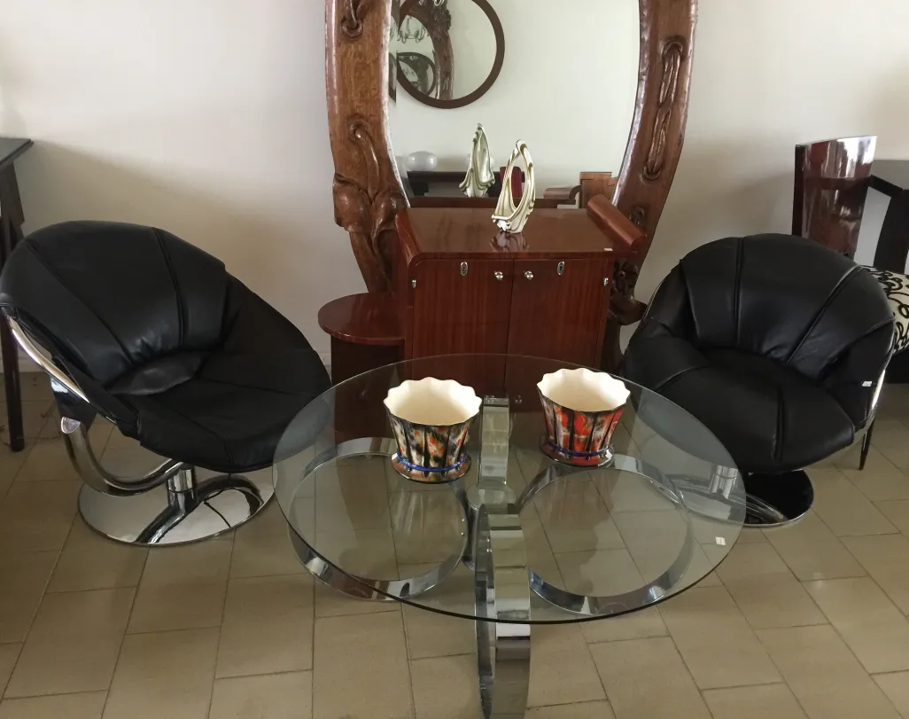 Mesa de centro antiga Art Deco com design elegante, acompanhada de cadeiras pretas em um ambiente moderno.