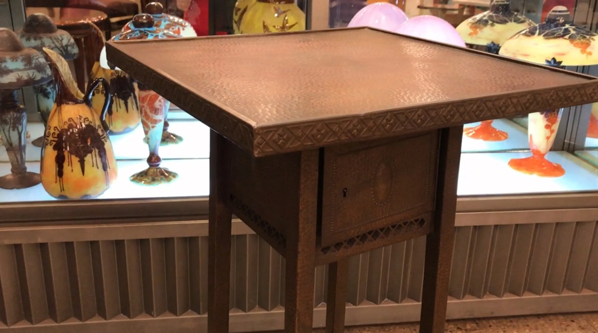 petite table ancienne avec design détaillé et vases colorés en arrière-plan