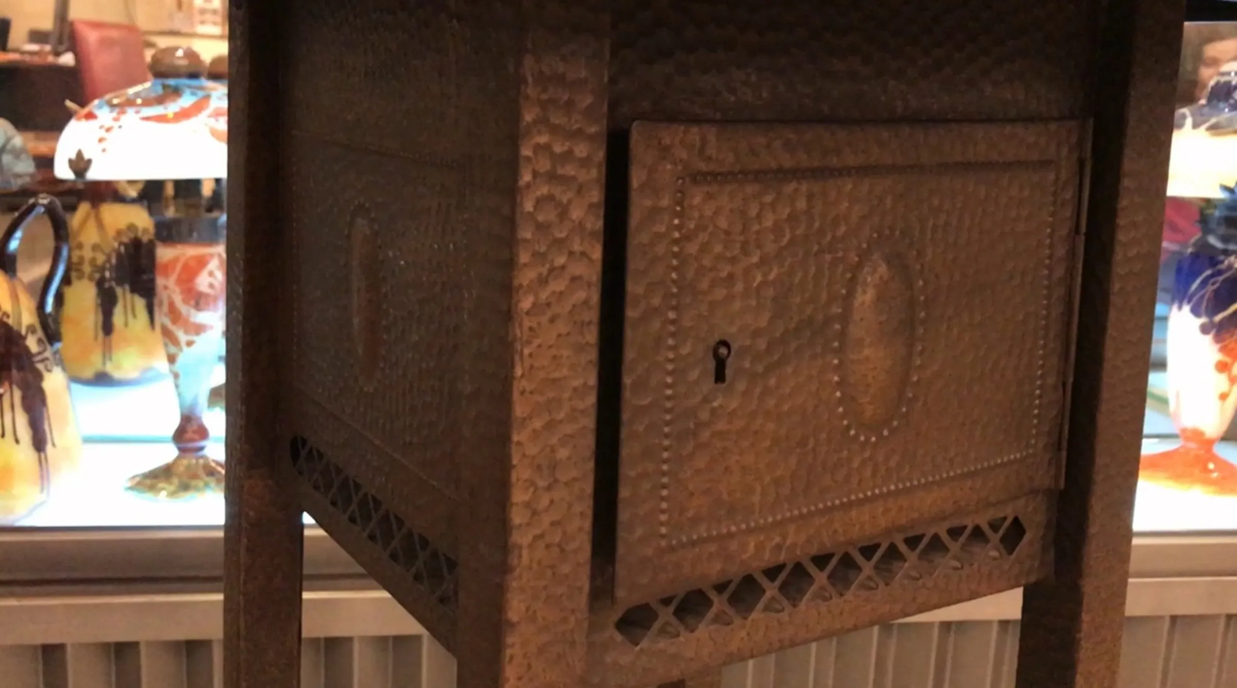 装飾デザインと前面の小さな引き出しを特徴とする古い小さなテーブルは、他の古物に囲まれています