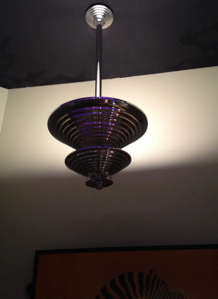 Lâmpada de teto antiga com design circular e estilo art deco, iluminando um ambiente neutro.