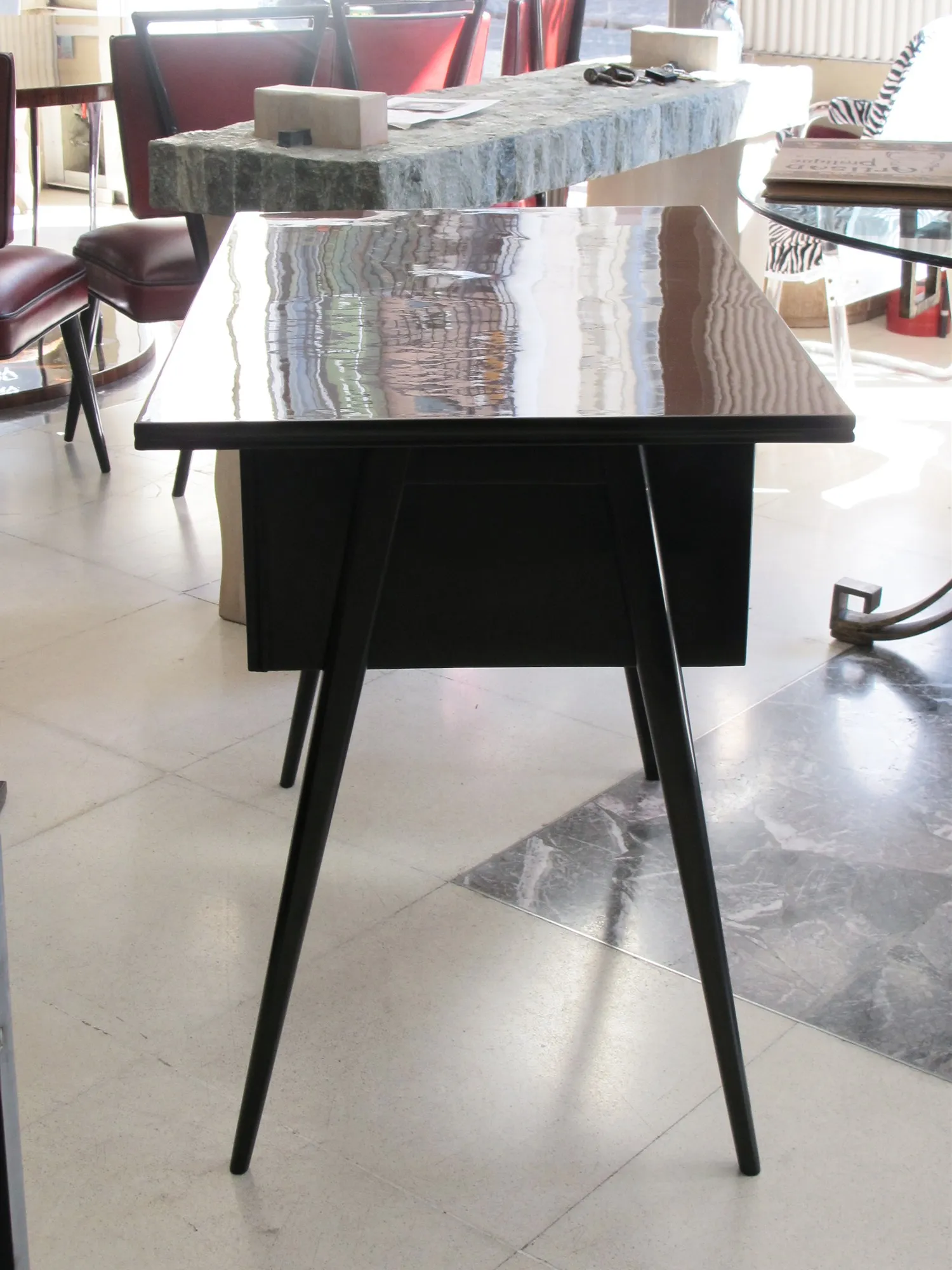 Bureau ancien au design minimaliste, pieds fins et surface brillante, entouré de meubles