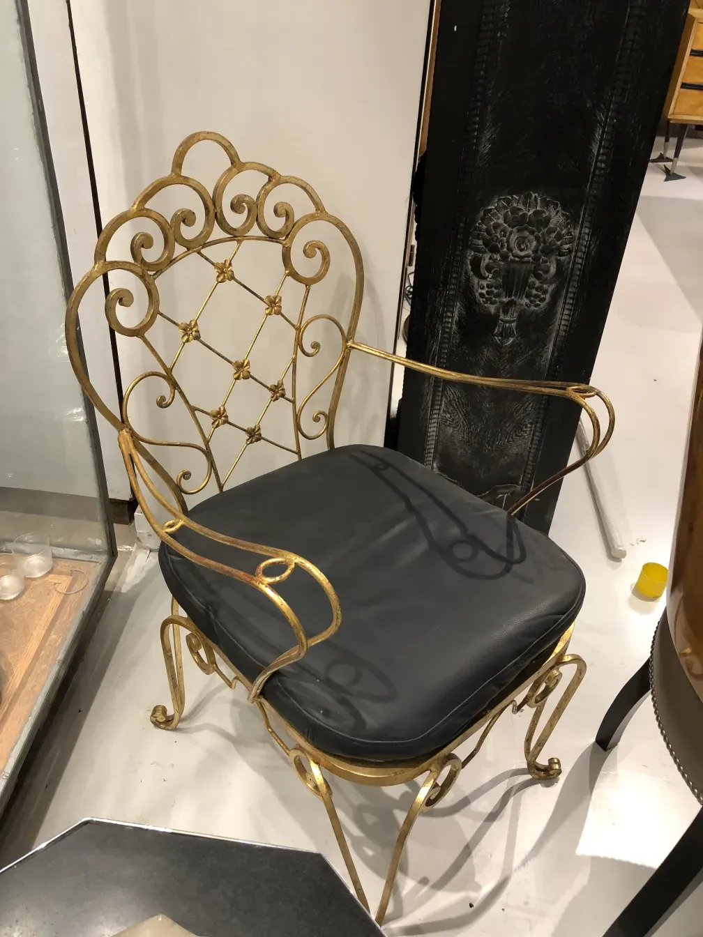 Due poltrone da giardino antiche con design art deco, con dettagli dorati e cuscini scuri, in un ambiente variegato.