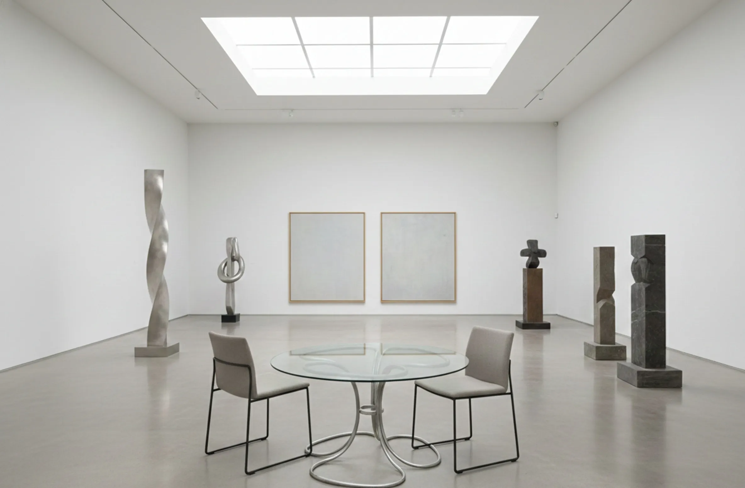 Tavolo da pranzo antico per sei persone in un ambiente minimalista con sculture moderne.