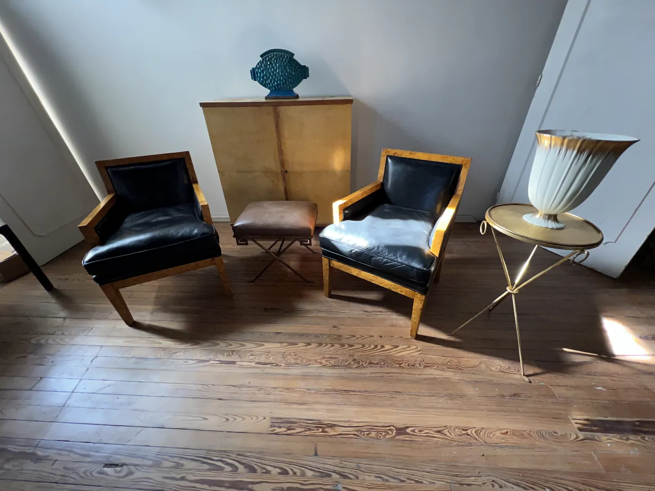 Duas poltronas antigas com assentos pretos, ao lado de uma mesa pequena.