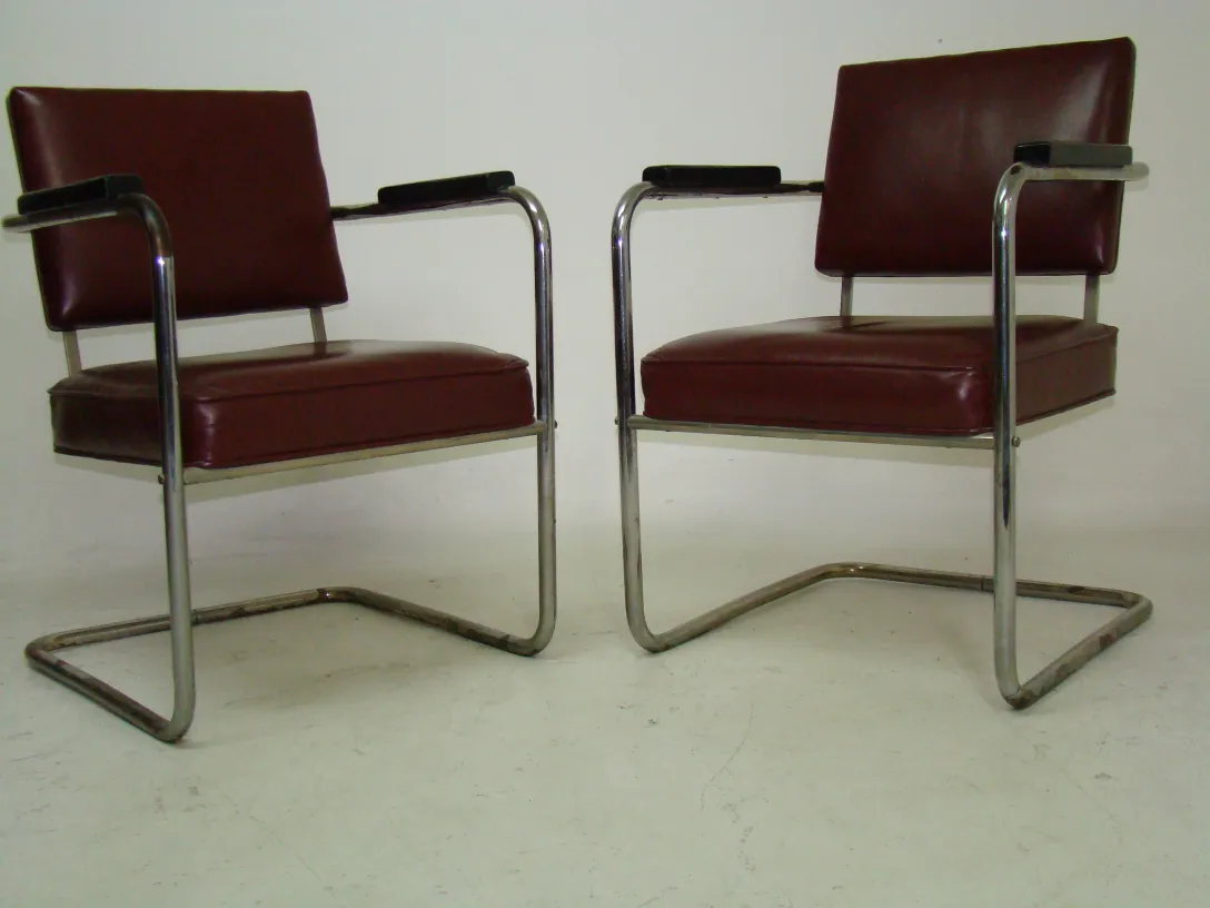 Duas poltronas antigas com estofamento vermelho em um fundo neutro.