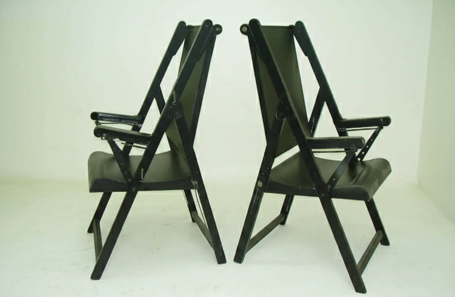 Duas poltronas antigas para serem restauradas, de cor escura em um fundo branco, com braços.