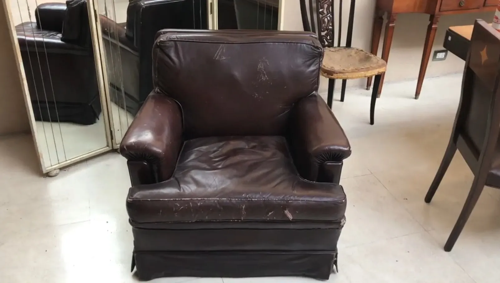 两张古董扶手椅显示出明显的磨损，周围是各种物品，位于修复环境中。