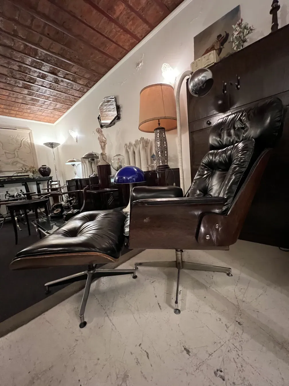 poltrona antiga Herman Miller aguardando restauração, em um ambiente com abajur e várias decorações.