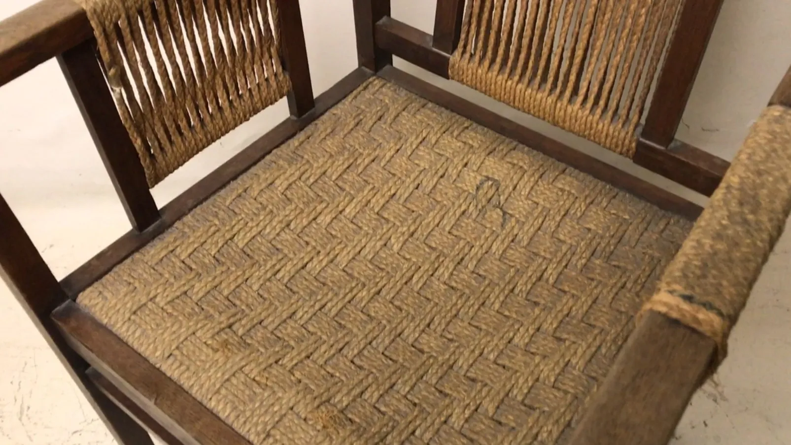 Sillón de escritorio antiguo con un diseño único y tejido en la base, rodeado de un ambiente clásico.