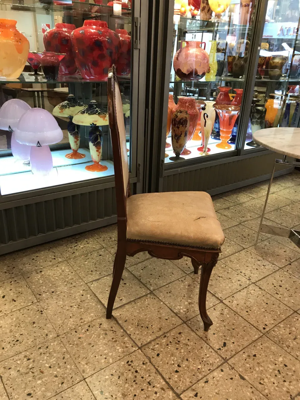 Silla antigua con tapizado neutro, fondo con objetos decorativos coloridos.