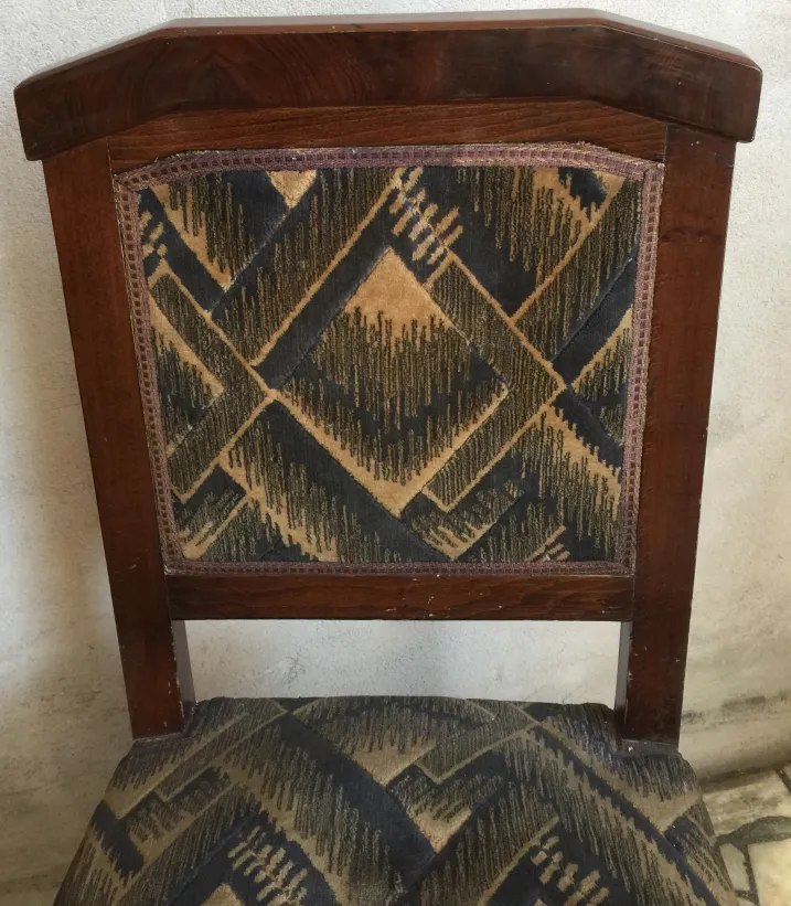Antique chairs with distinctive design and visible wear on upholstery in a neutral setting.