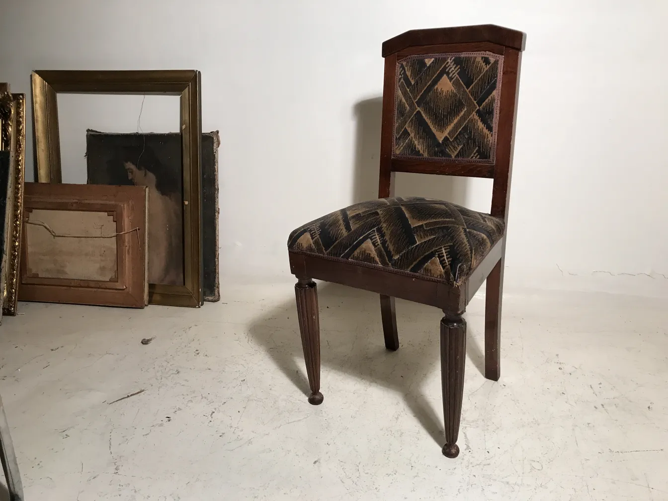 Side view of 2 antique chairs with an attractive design and an artistic background of paintings.