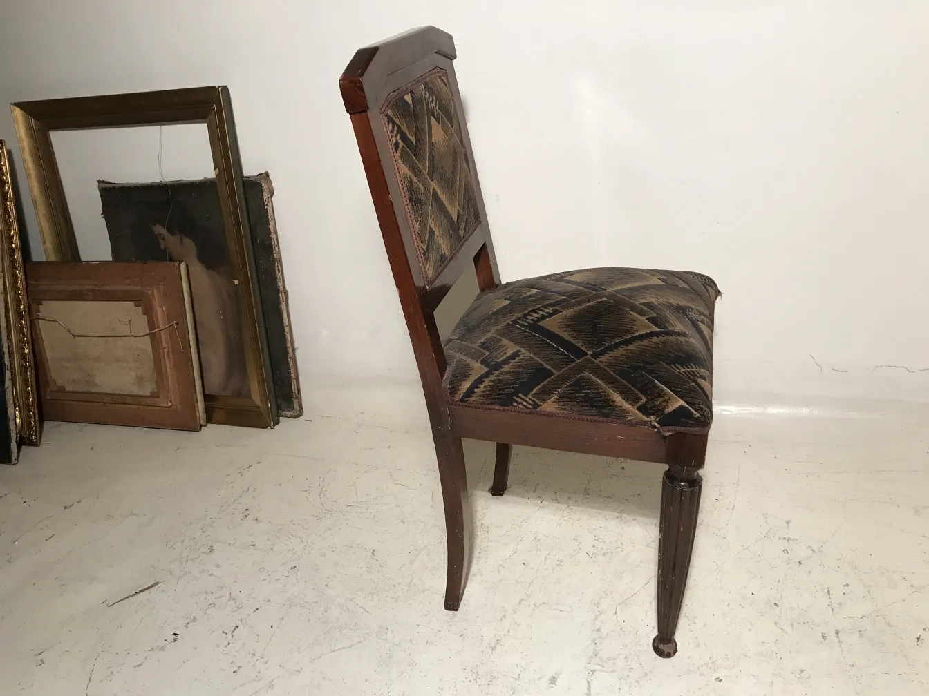 Duas cadeiras antigas com design art deco, adequadas para restauração. Fundo com molduras de quadros.